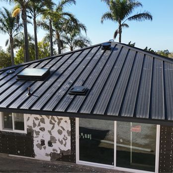 Gray metal roof on a white house with a gutter and a chimney, trees in the background. Gray metal roof on a white house with a gutter and a chimney, trees in the background.