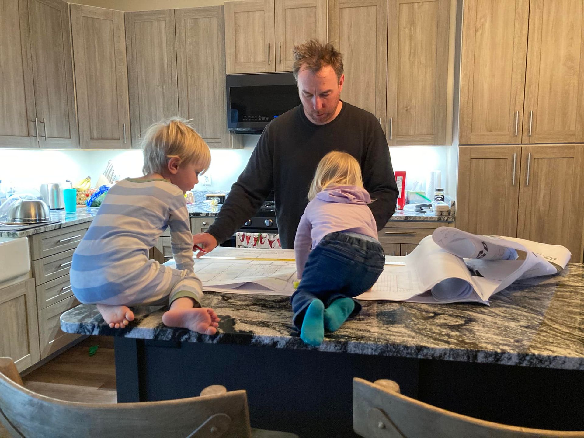 A man and two young children looking at plans on a kitchen counter.