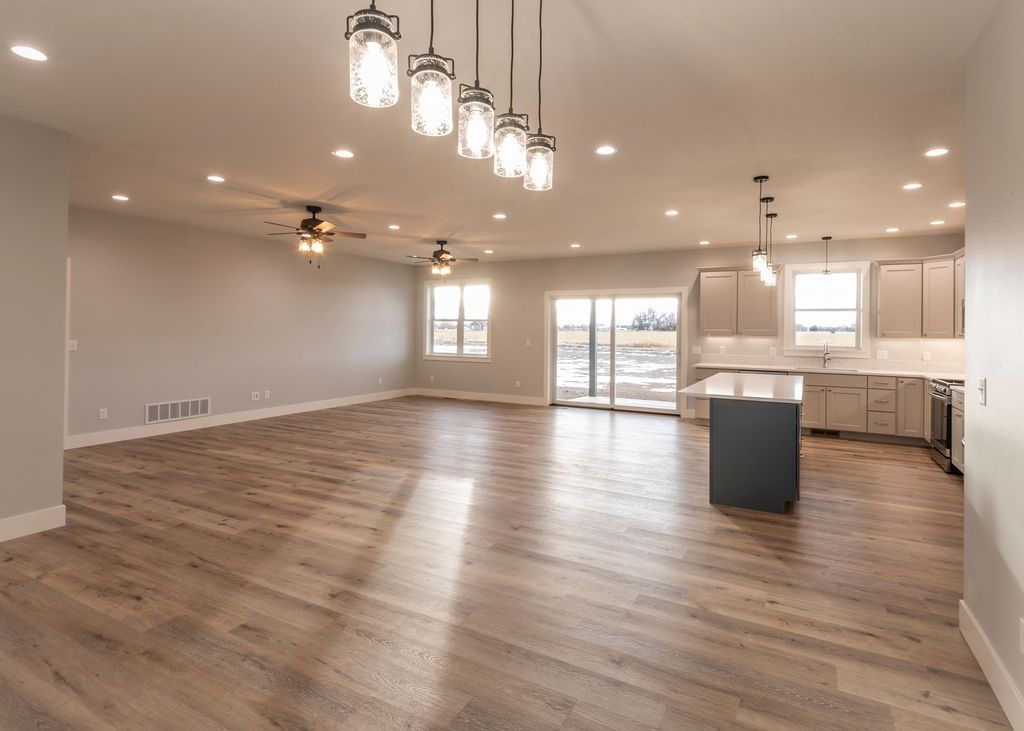 Spacious, empty, modern home interior with wood floors and open kitchen; neutral tones.