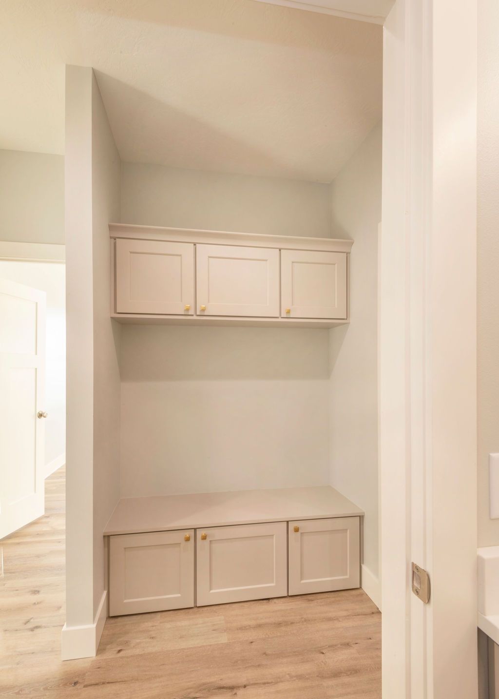 Built-in white cabinets and bench in a light-colored room; wooden floor and neutral walls.