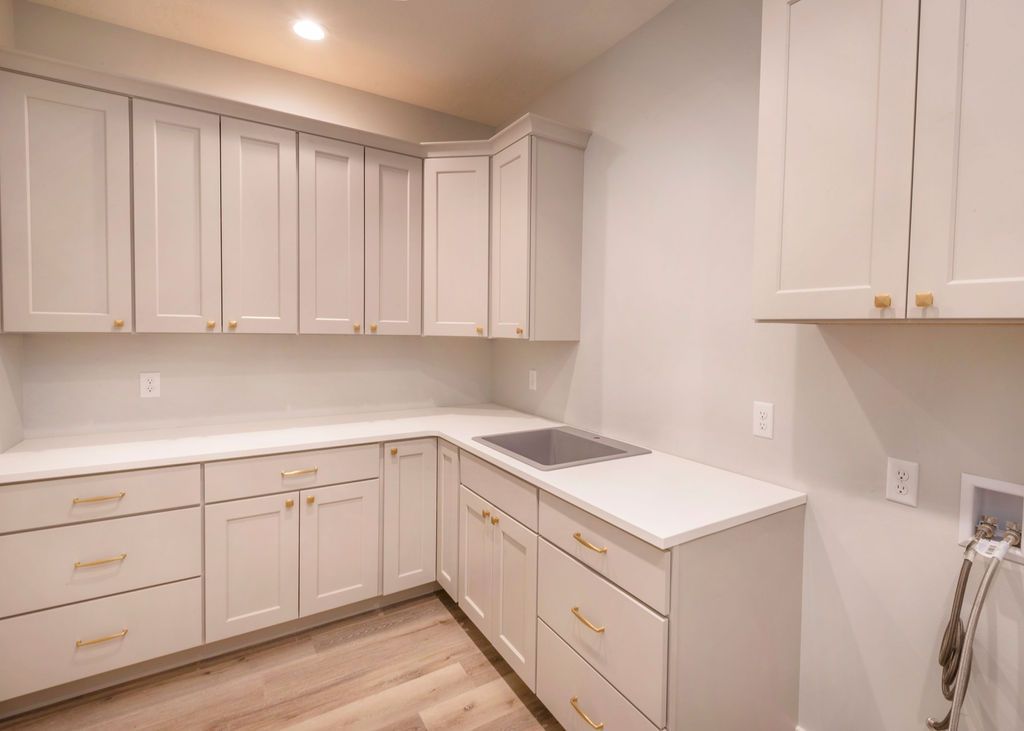 Light gray kitchen with white countertops, gold hardware, and light wood floors.