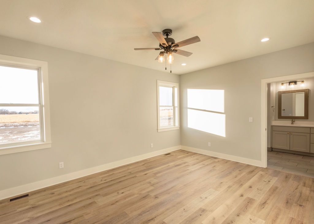 Empty bedroom with light wood floors, pale gray walls, and a bathroom entrance.
