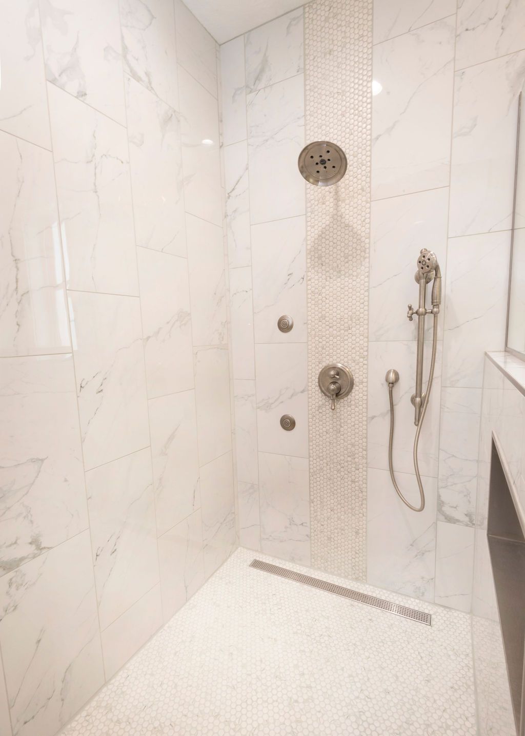 White tiled shower with multiple shower heads and a handheld wand.