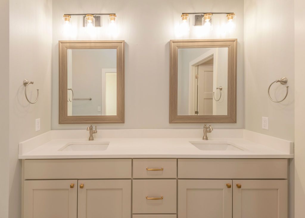 Bathroom with dual sinks, beige cabinets, gold fixtures, two mirrors, and sconce lighting.