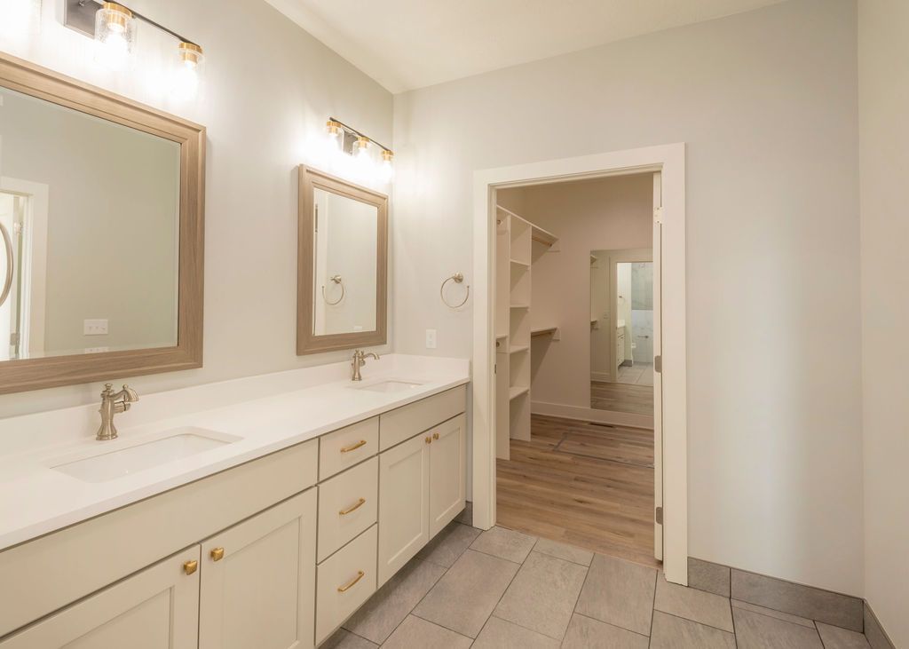 Bathroom with double vanity, mirrors, and walk-in closet entrance; neutral colors and modern design.