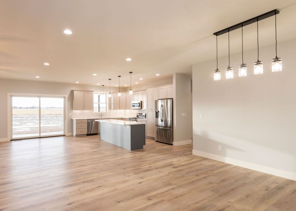Open-concept kitchen and dining area with light wood floors, stainless steel appliances, and a modern light fixture.