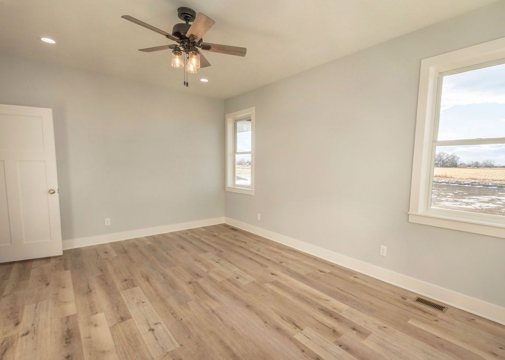 Empty bedroom with light wood floor, pale blue walls, white trim, two windows.