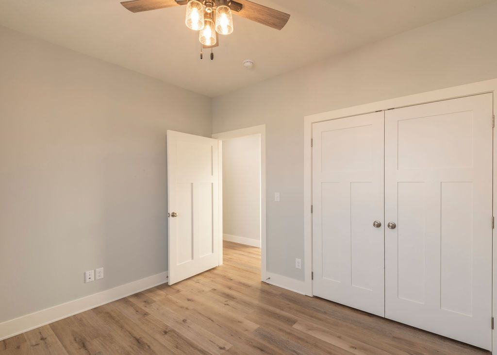 Empty bedroom with light wood floors, white doors and trim, and a ceiling fan.
