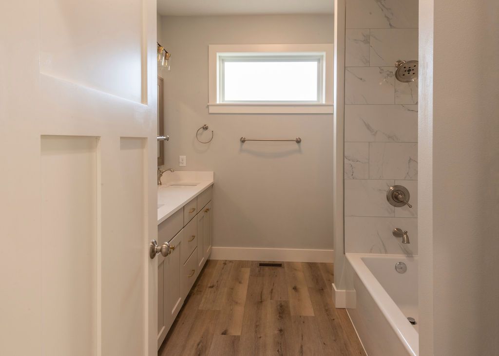 Bathroom with white cabinets, a bathtub, and a window. Light-colored wood-look flooring.