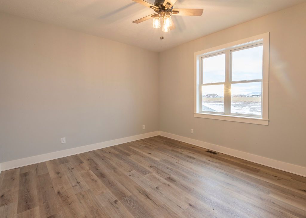 Empty bedroom with light wood-look floor, window, neutral walls, and ceiling fan.