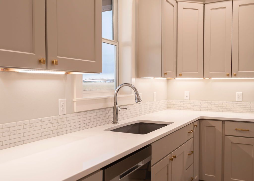 Beige kitchen with cabinets, sink, and countertop. Window in background.