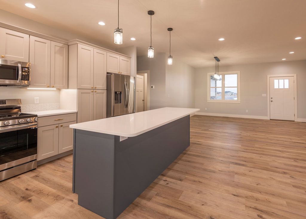 Modern kitchen with light cabinets, stainless steel appliances, gray island, and wood floors.