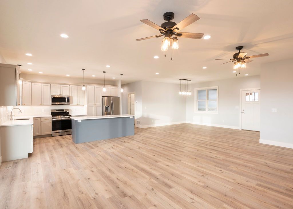 Open-concept kitchen and living area with gray cabinetry, blue island, light wood floors, and two ceiling fans.