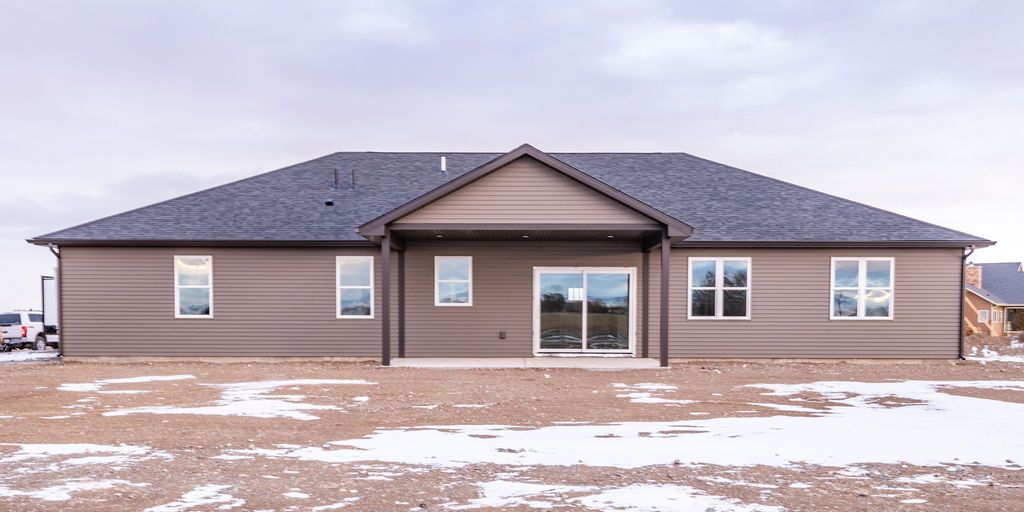 Back view of a single-story house with brown siding and a dark gray roof. Snowy, barren yard in the foreground.