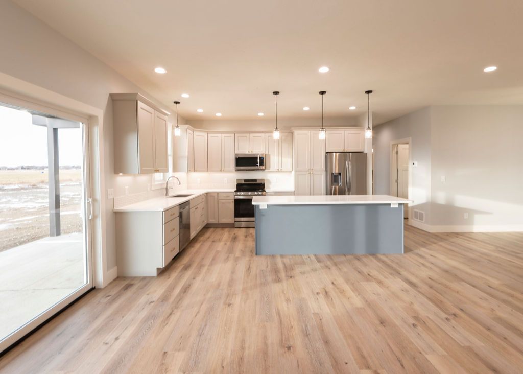 Open-concept kitchen with light gray cabinets, blue island, stainless steel appliances, and wood flooring.