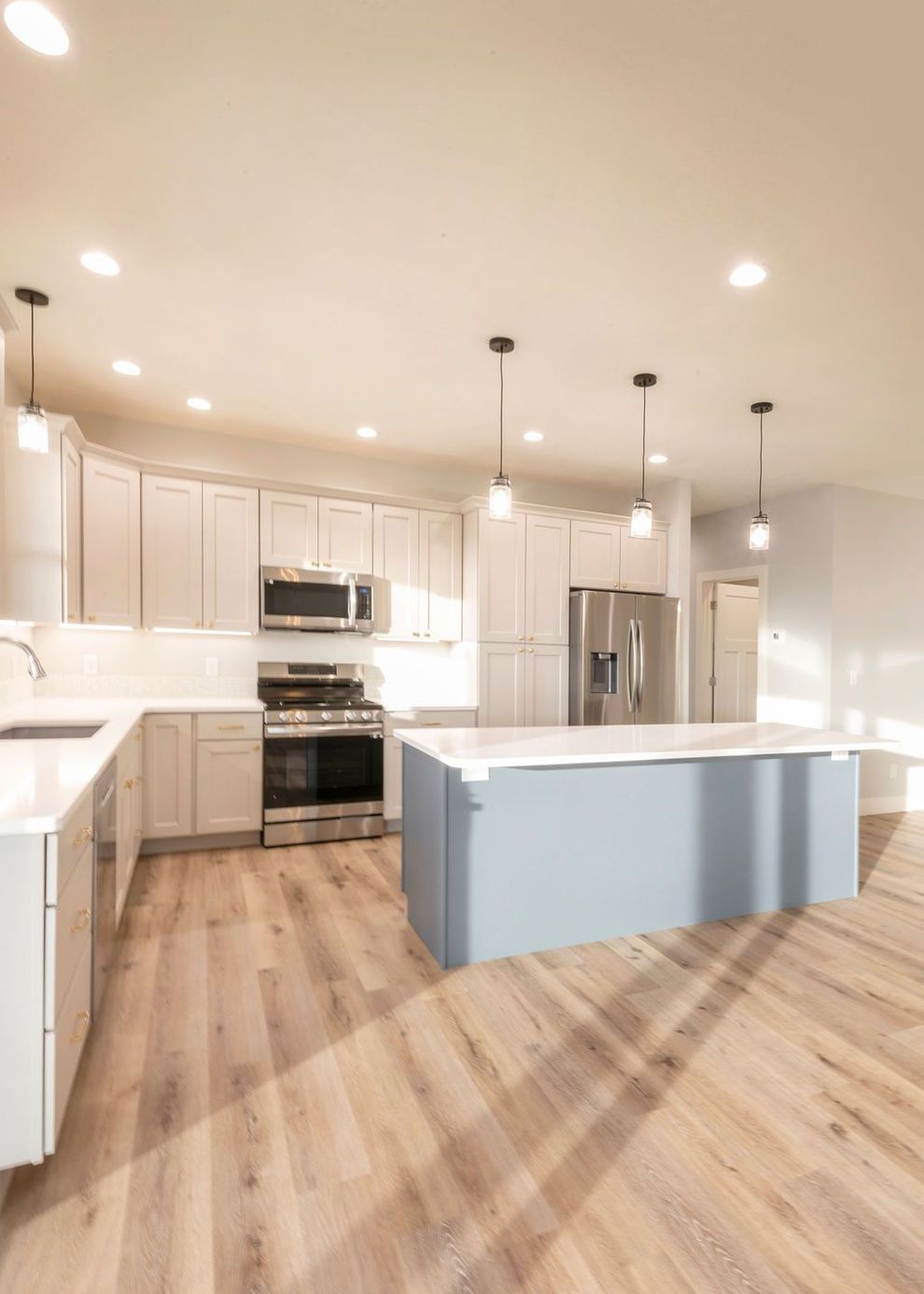Spacious modern kitchen with light wood floors, white cabinets, blue island, stainless appliances, and recessed lighting.