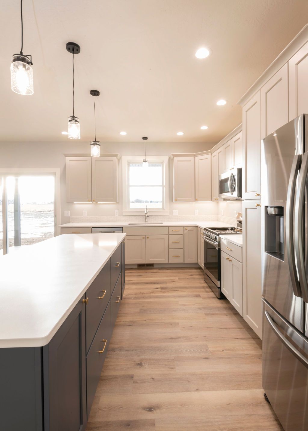 Modern kitchen with white cabinets, gray island, stainless steel appliances, and wood floors.