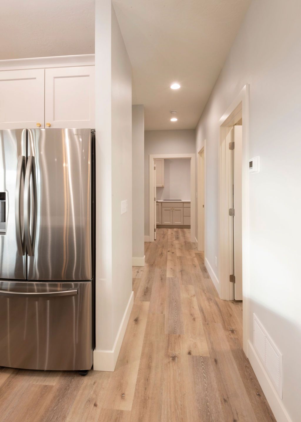 Long, light-filled hallway with light wood floors, and a stainless steel fridge.