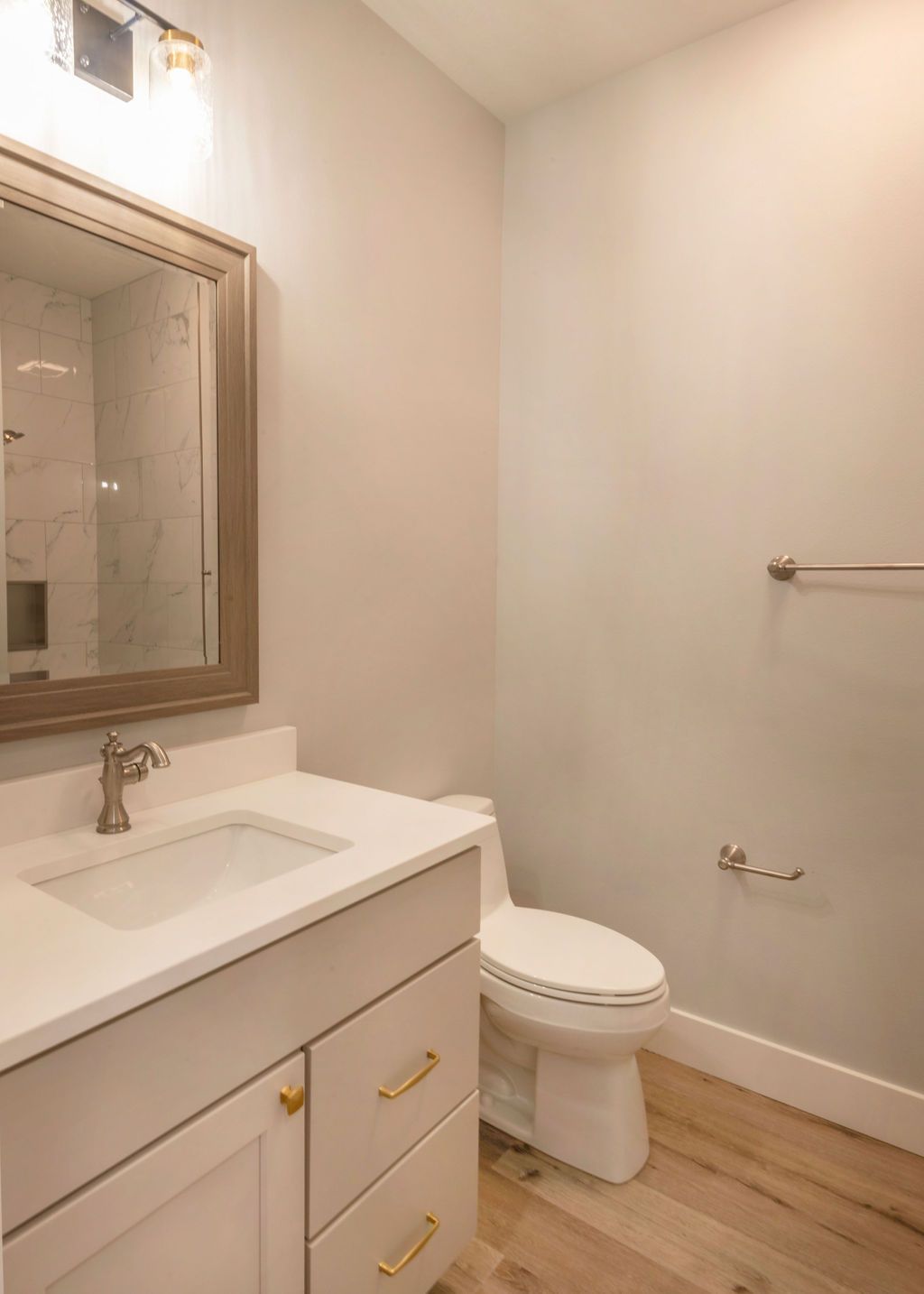 Bathroom with white vanity, toilet, mirror, brushed gold hardware, and light wood flooring.