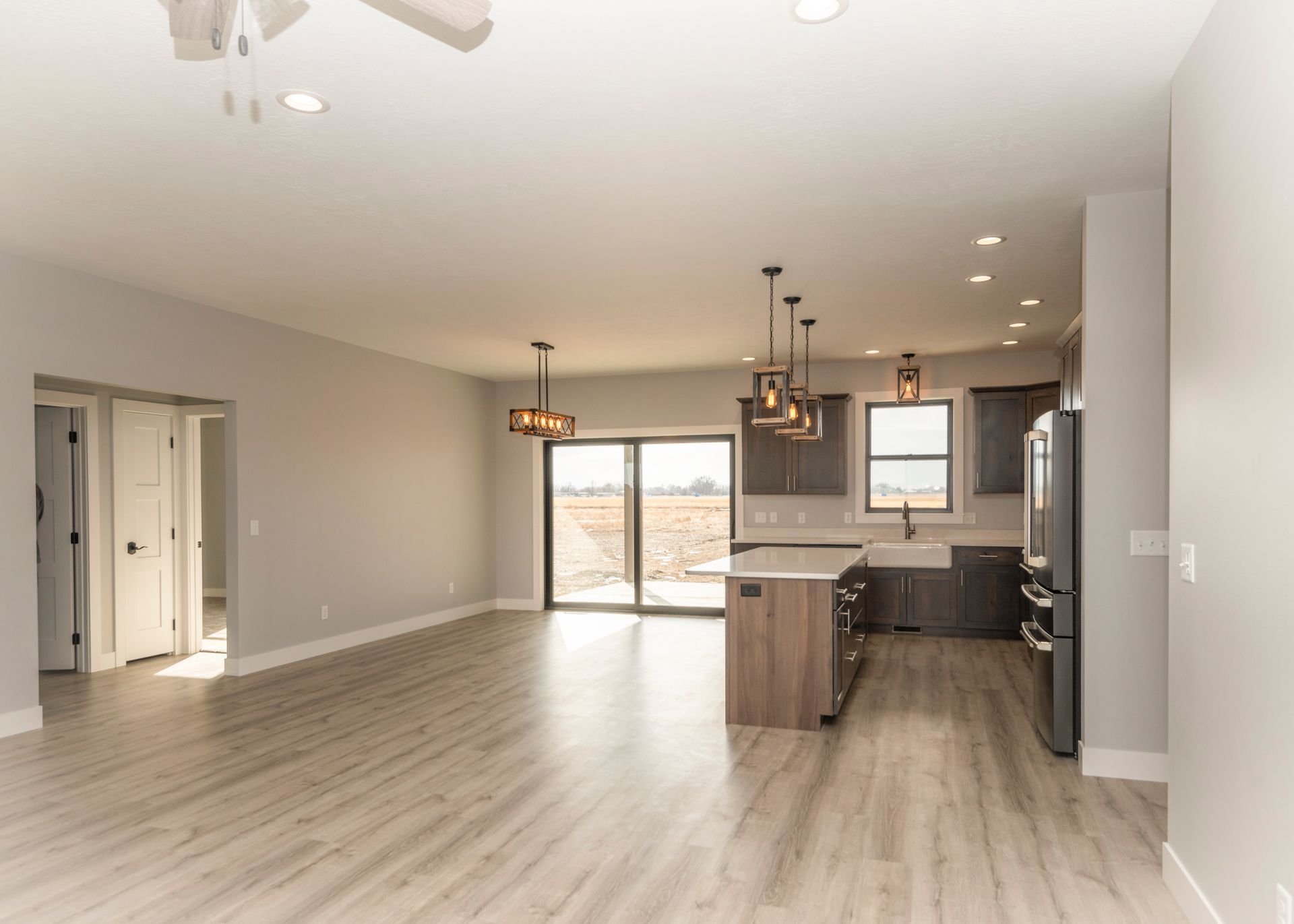 Open-concept kitchen and living area with light wood floors, gray cabinets, and sliding glass doors.