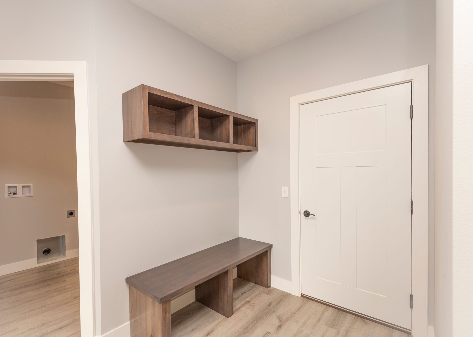 Mudroom with wooden bench, floating shelves, and white door.
