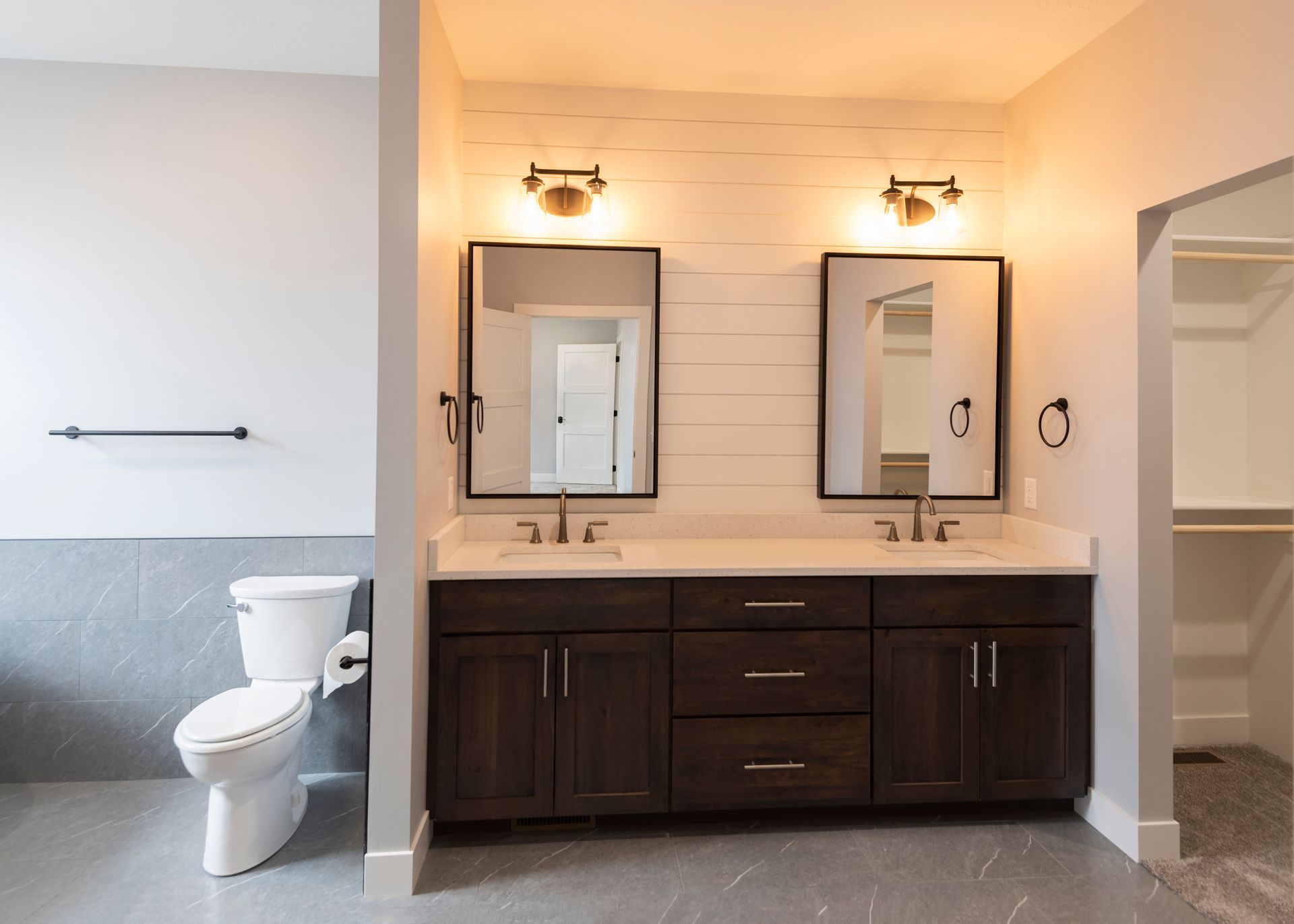 Bathroom with a double vanity, dark wood cabinets, mirrors, and a toilet. Includes a walk-in closet entrance.