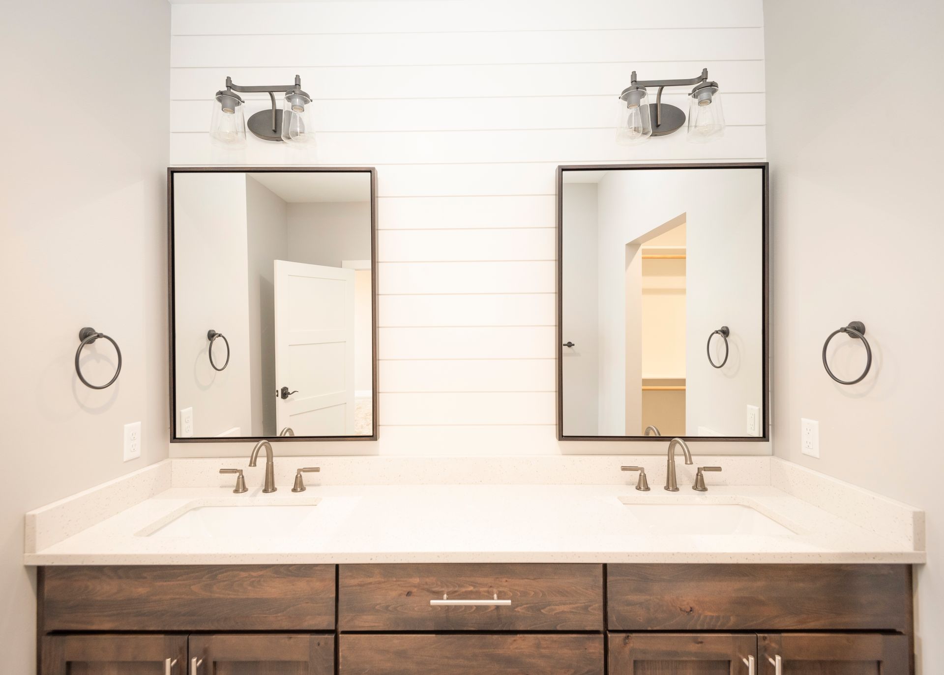 Bathroom with two sinks, mirrors, and sconces, against a shiplap wall.