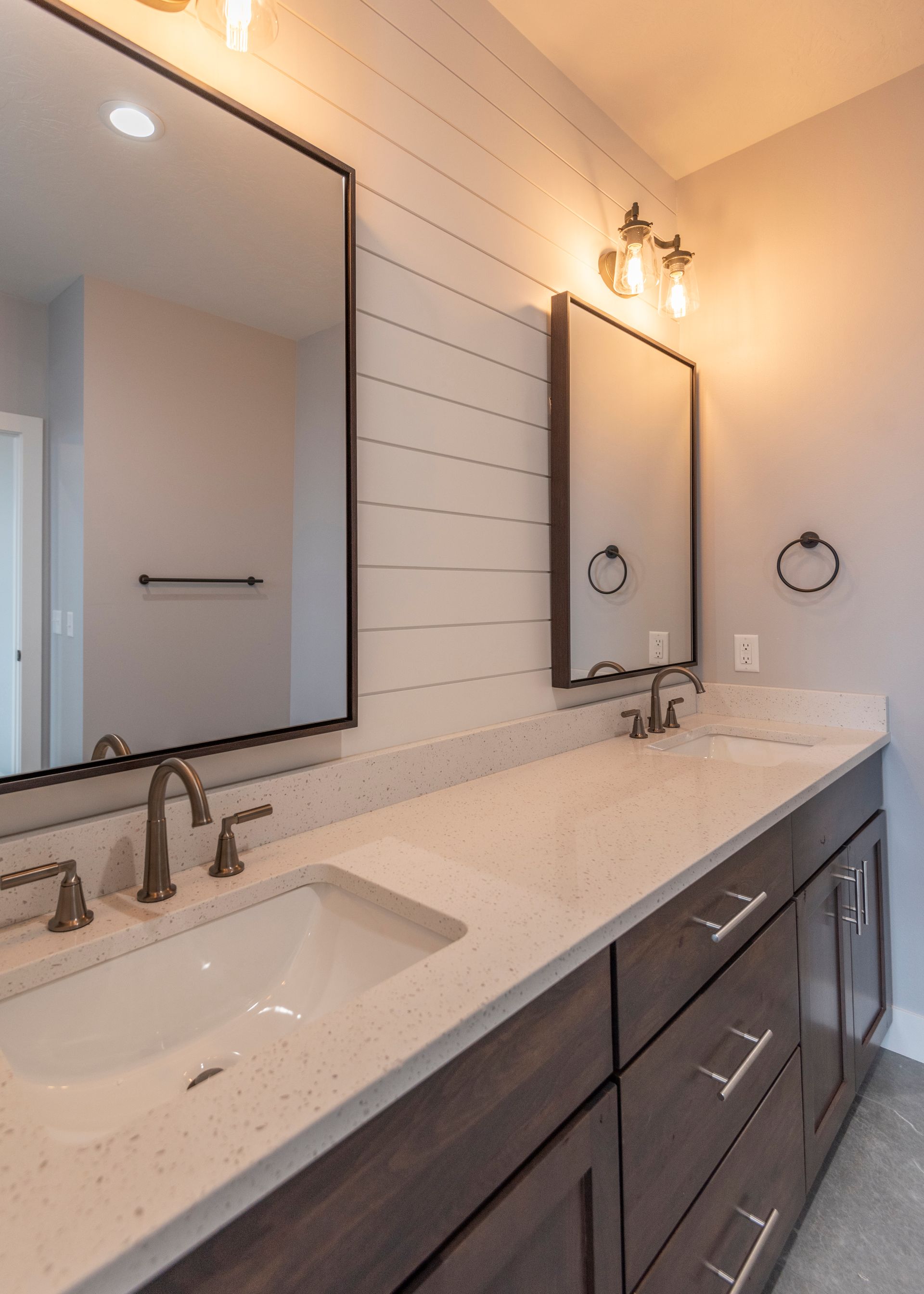 Bathroom with dual sinks, dark wood vanity, white countertop, and shiplap wall.