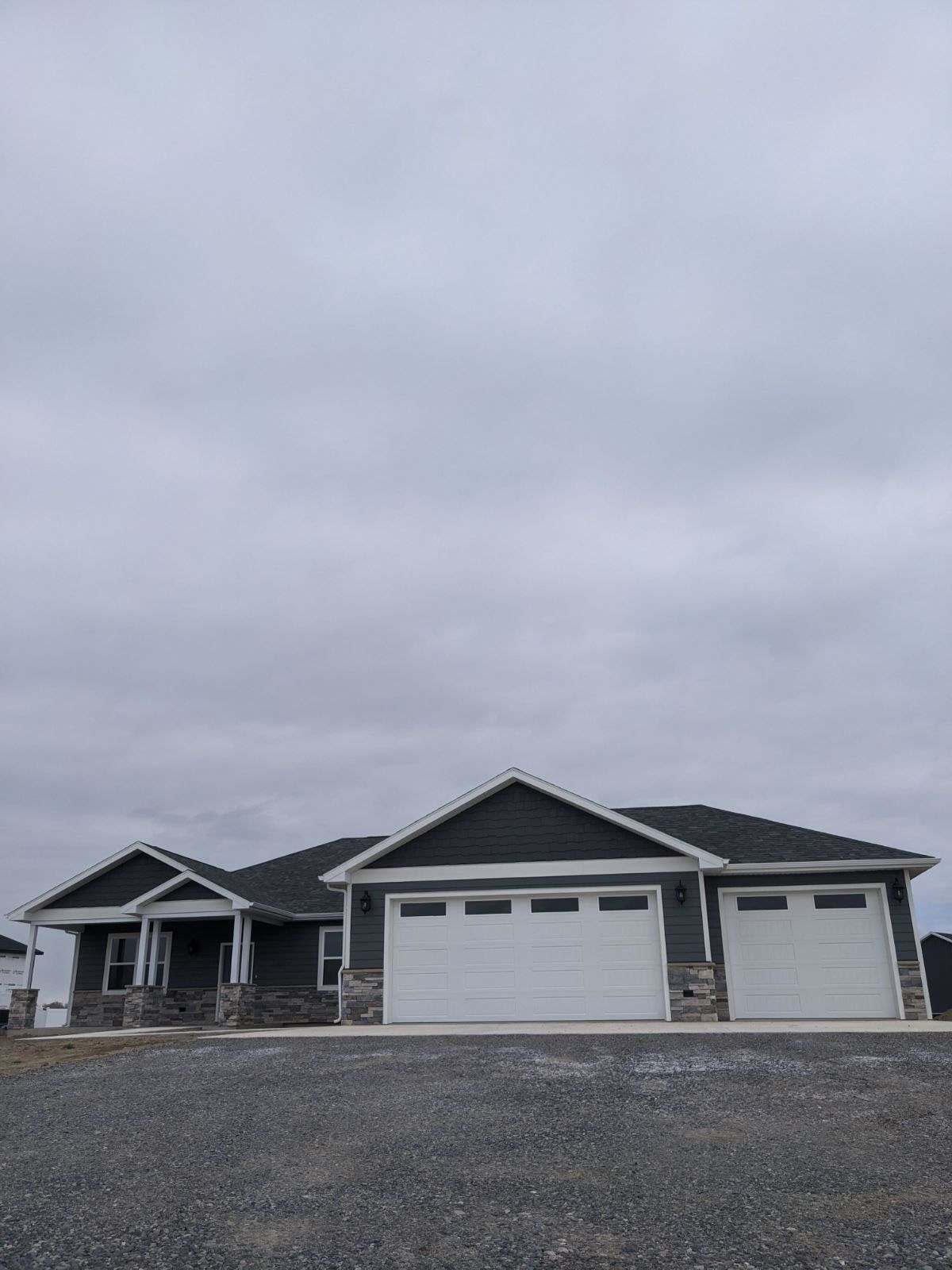 Gray house with white garage doors and stone accents under a cloudy sky.