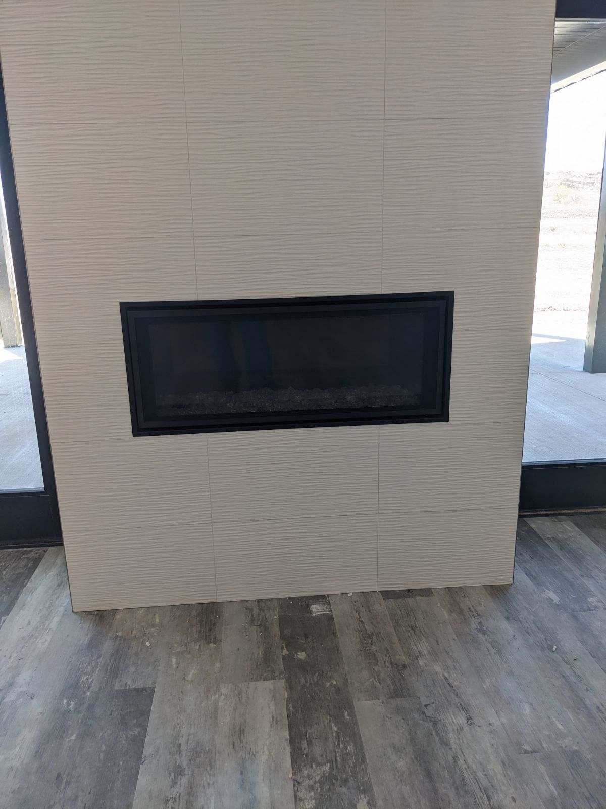 Fireplace with black insert, cream-colored textured wall, set against wood-like flooring.