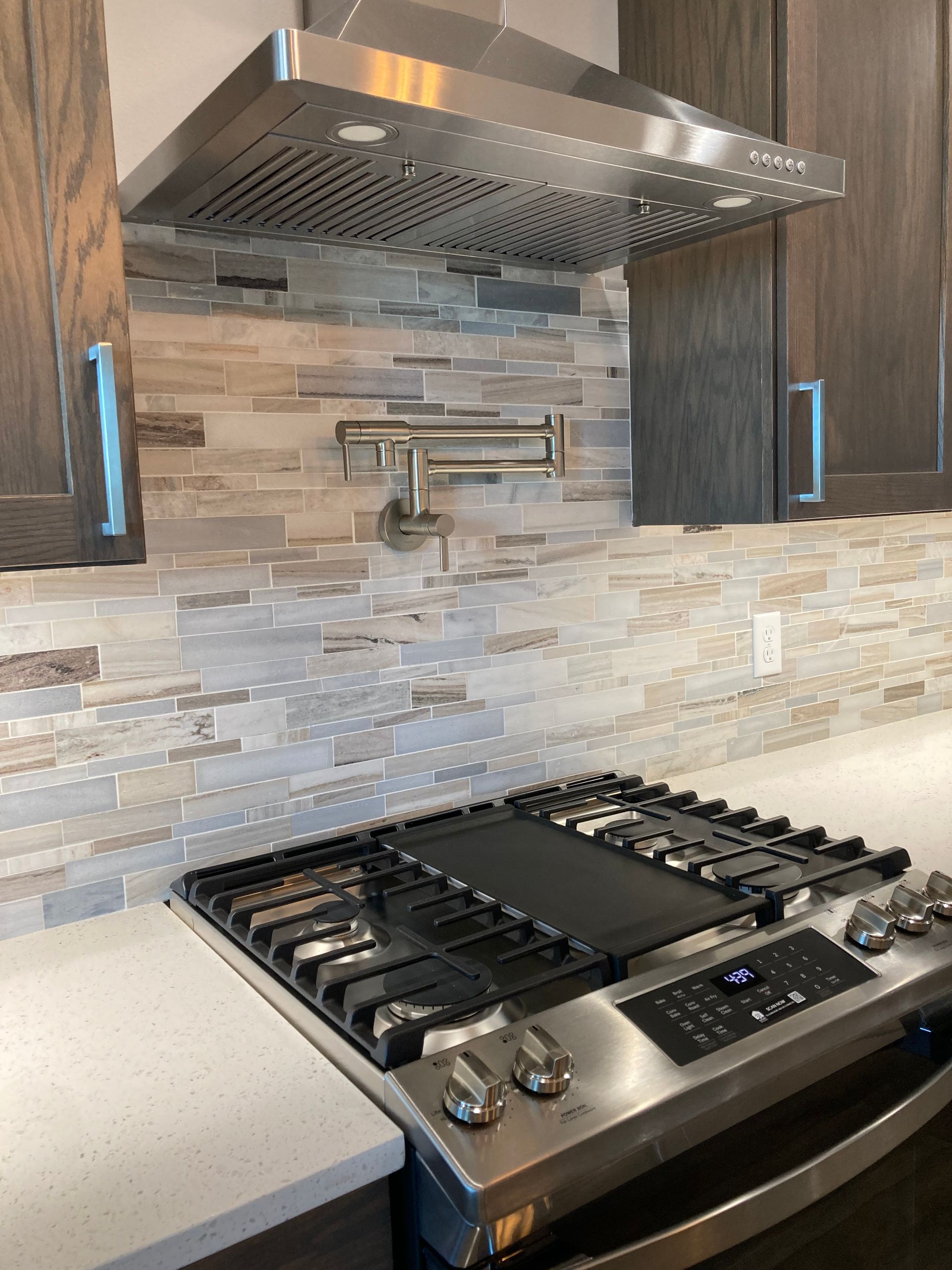 Stainless steel range with hood, backsplash, and pot filler in kitchen.