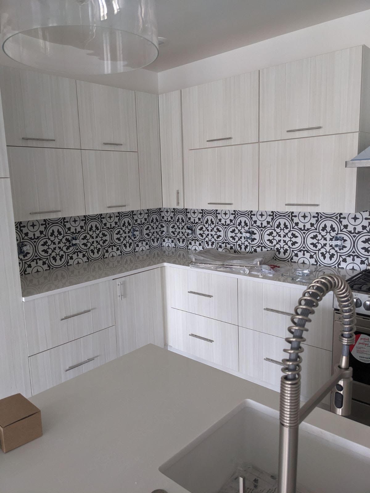 Modern kitchen with white cabinets, patterned backsplash, and stainless steel faucet.