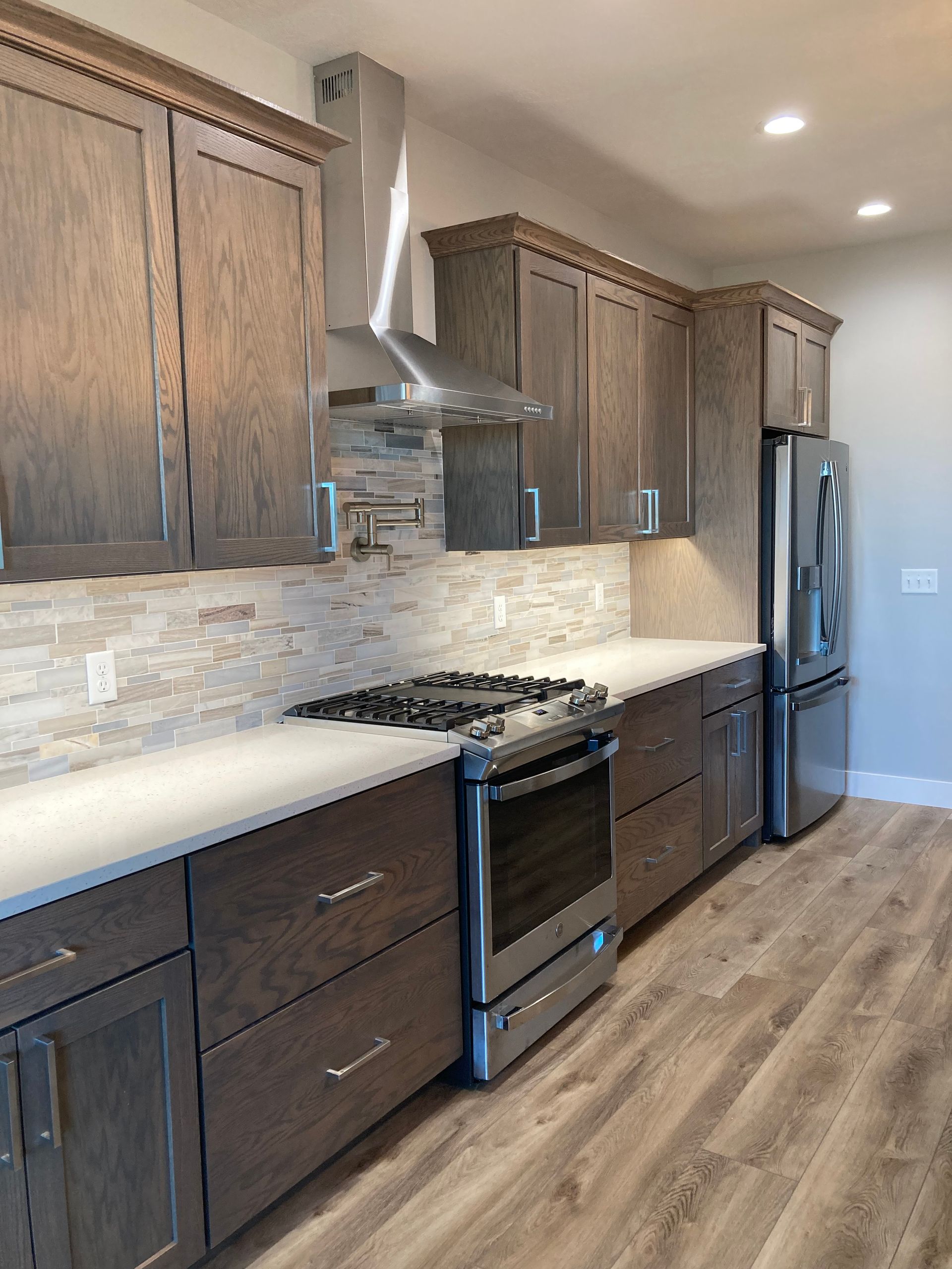 Kitchen with gray-brown cabinets, light countertops, stainless steel appliances, and a light stone backsplash.