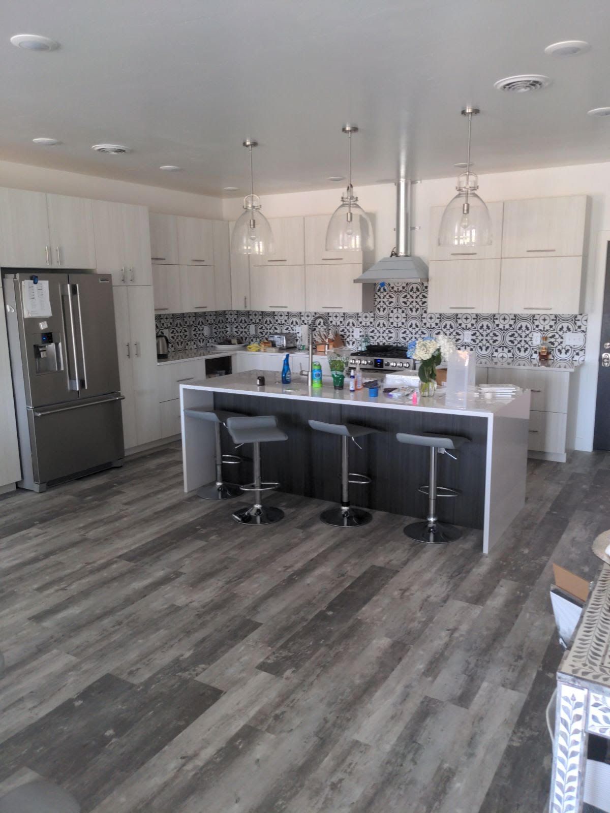 Modern kitchen with light grey cabinets, dark grey island with stools, and silver appliances.