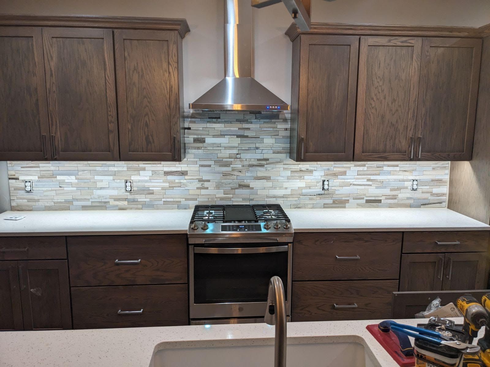 Kitchen with dark brown cabinets, stone backsplash, and stainless steel appliances.