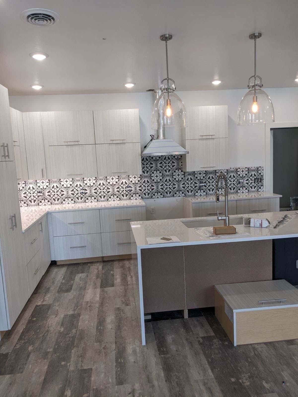 Modern kitchen with white cabinets, patterned backsplash, and island with two pendant lights.