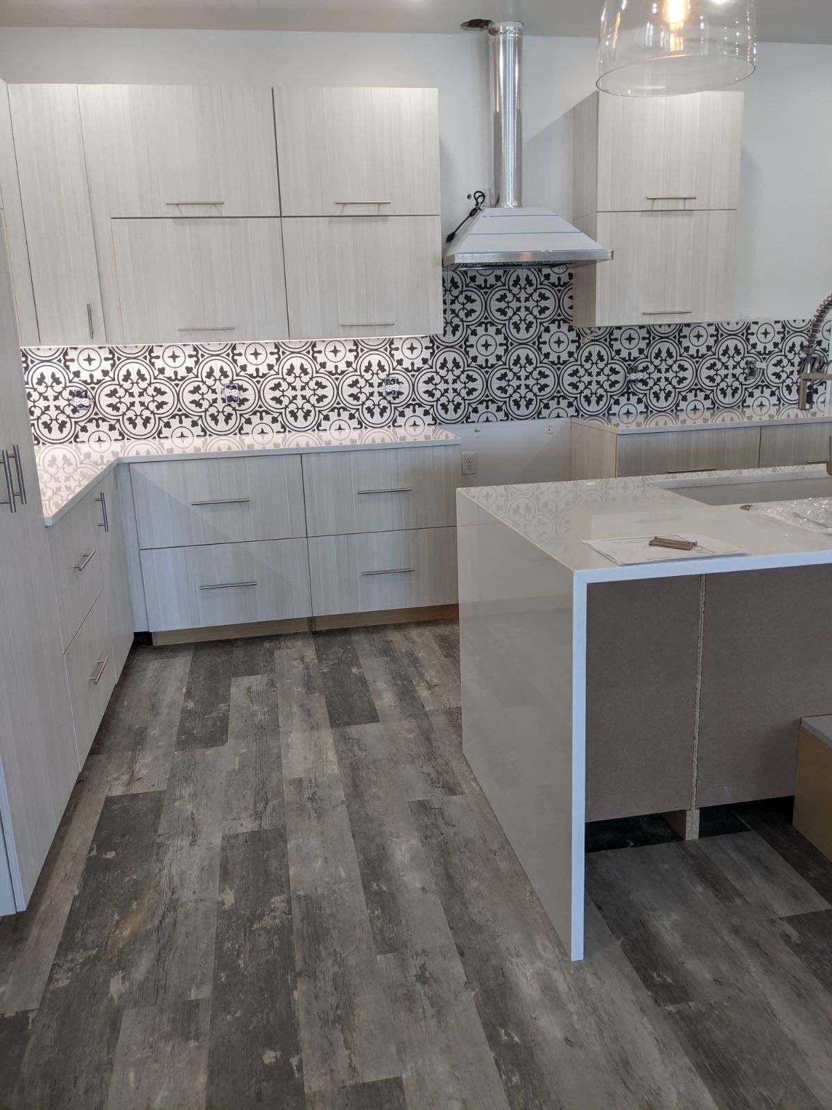 Modern kitchen with light wood cabinets, patterned backsplash, and gray flooring.