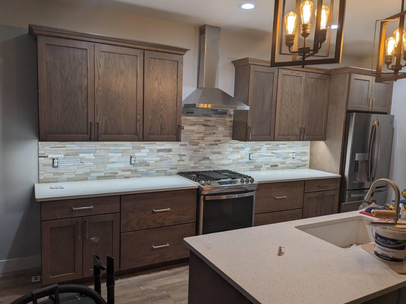 Kitchen with dark wood cabinets, stone backsplash, stainless steel hood, and white countertops.