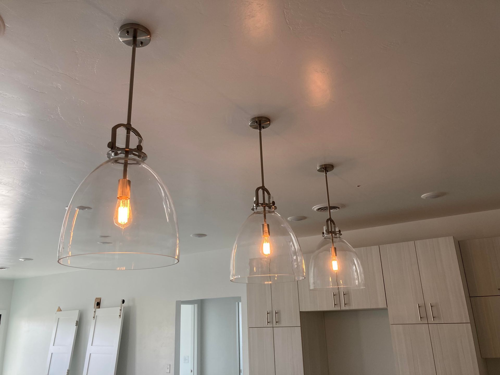Three clear glass pendant lights hanging from a white ceiling in a kitchen.