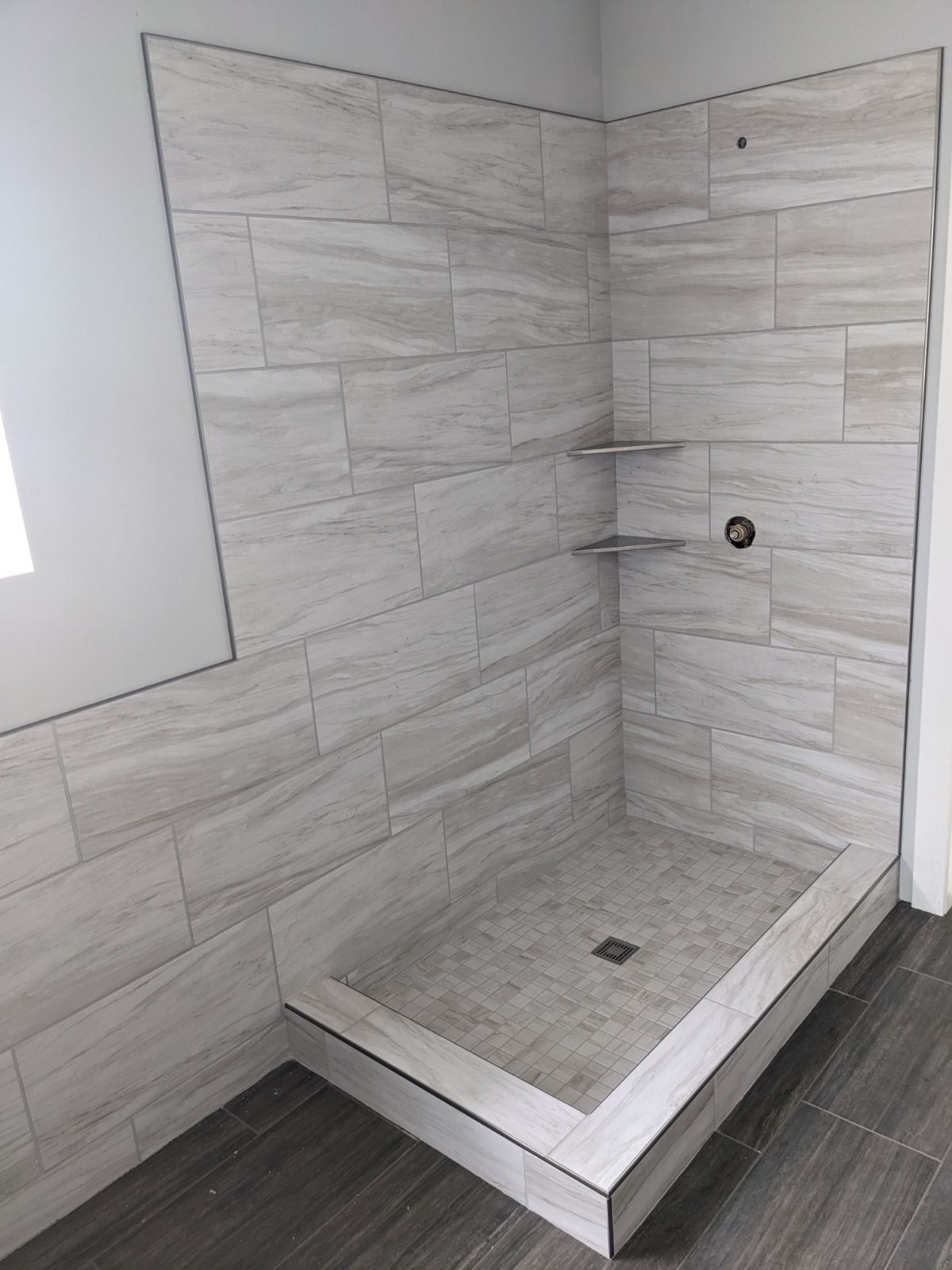 Tile-walled shower stall with built-in shelves, a gray base, and gray and white tile.