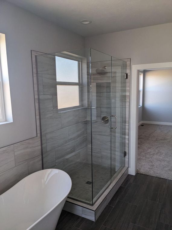 Modern bathroom with glass shower, soaking tub, and open doorway to a bedroom. Grey and white tones.