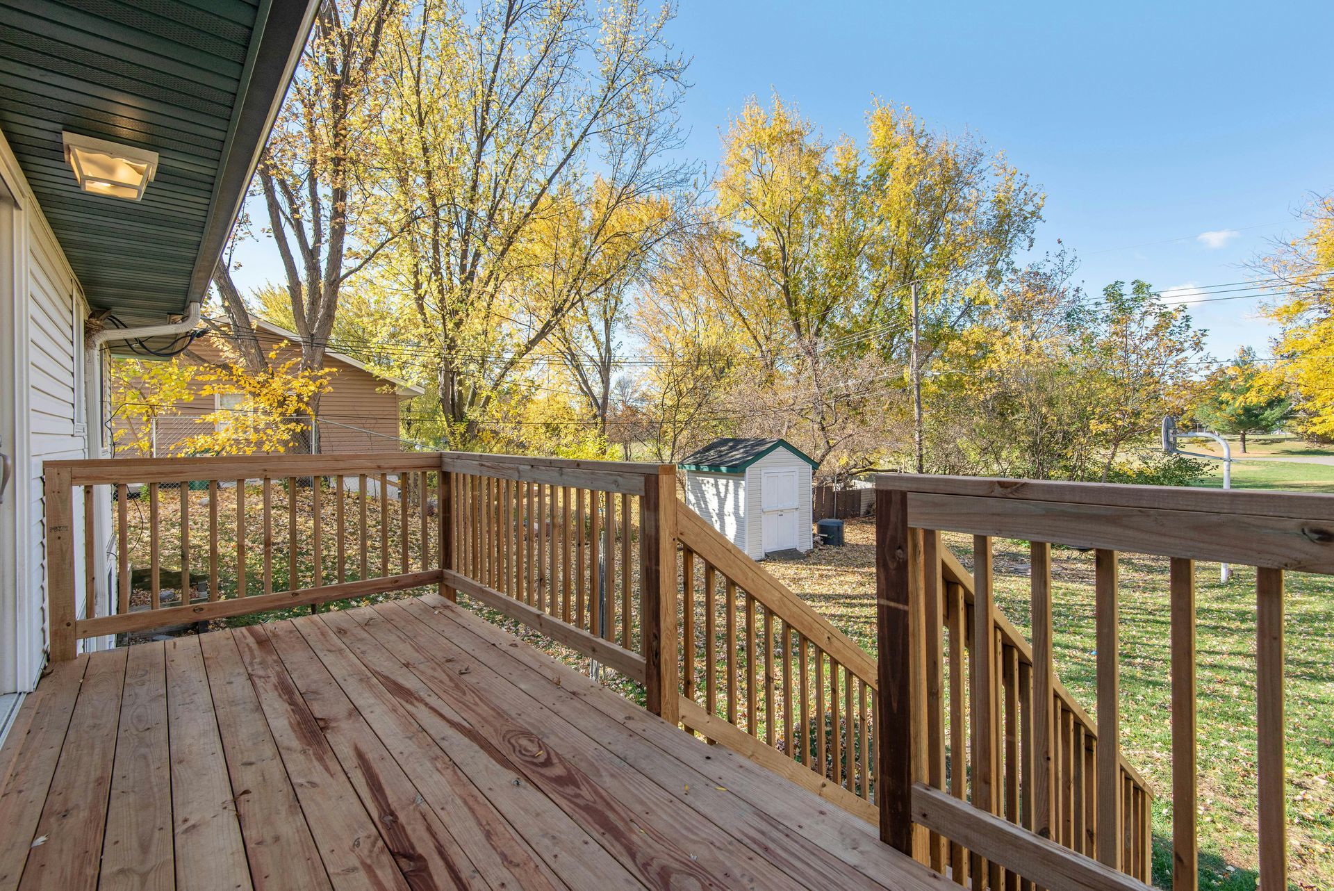 Wooden backyard deck with railing, steps, and autumn trees under a blue sky