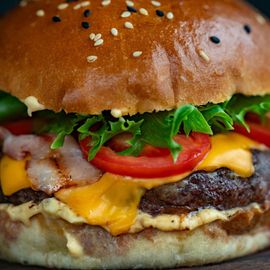 A close up of a hamburger with cheese , tomatoes , lettuce and bacon on a bun.