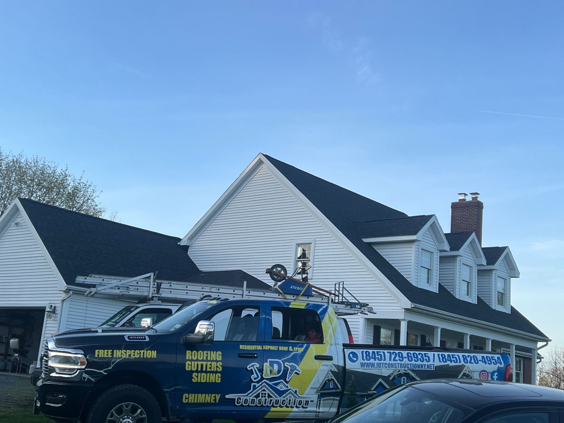 Black roofing installed on a white house, contractor truck parked in front.