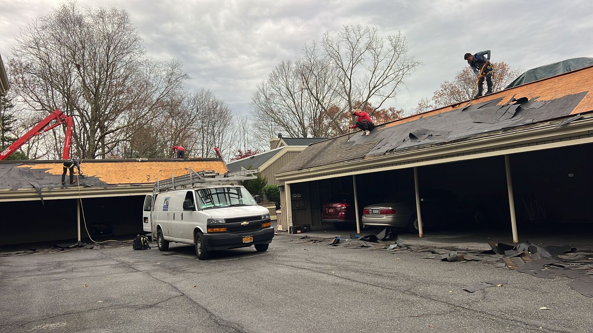 Roofers removing old shingles from a building with a white van parked in front.