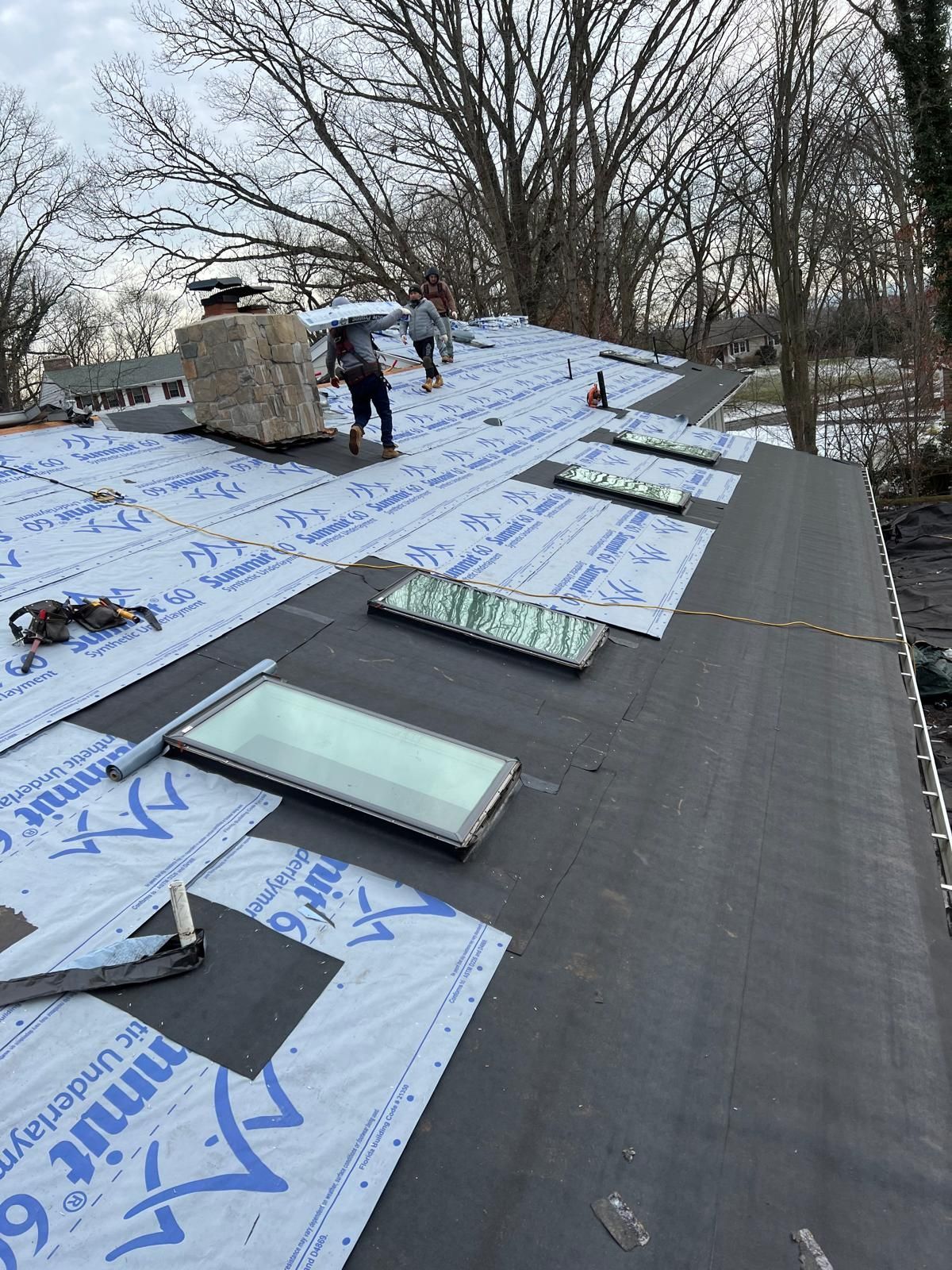 Roofing crew on a partially completed roof with skylights and chimney.