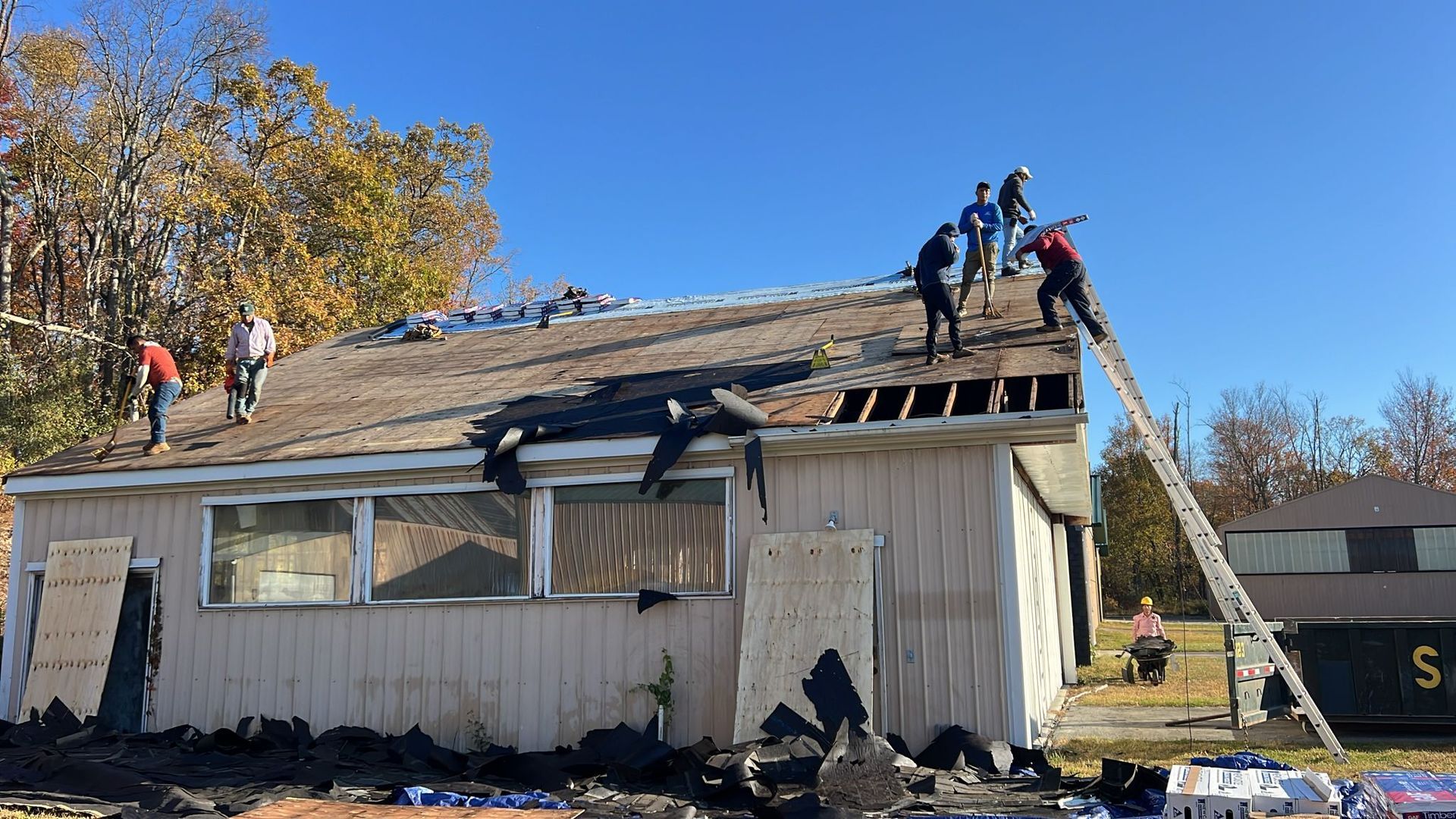 People removing a roof from a small building on a sunny day. A ladder is propped up.