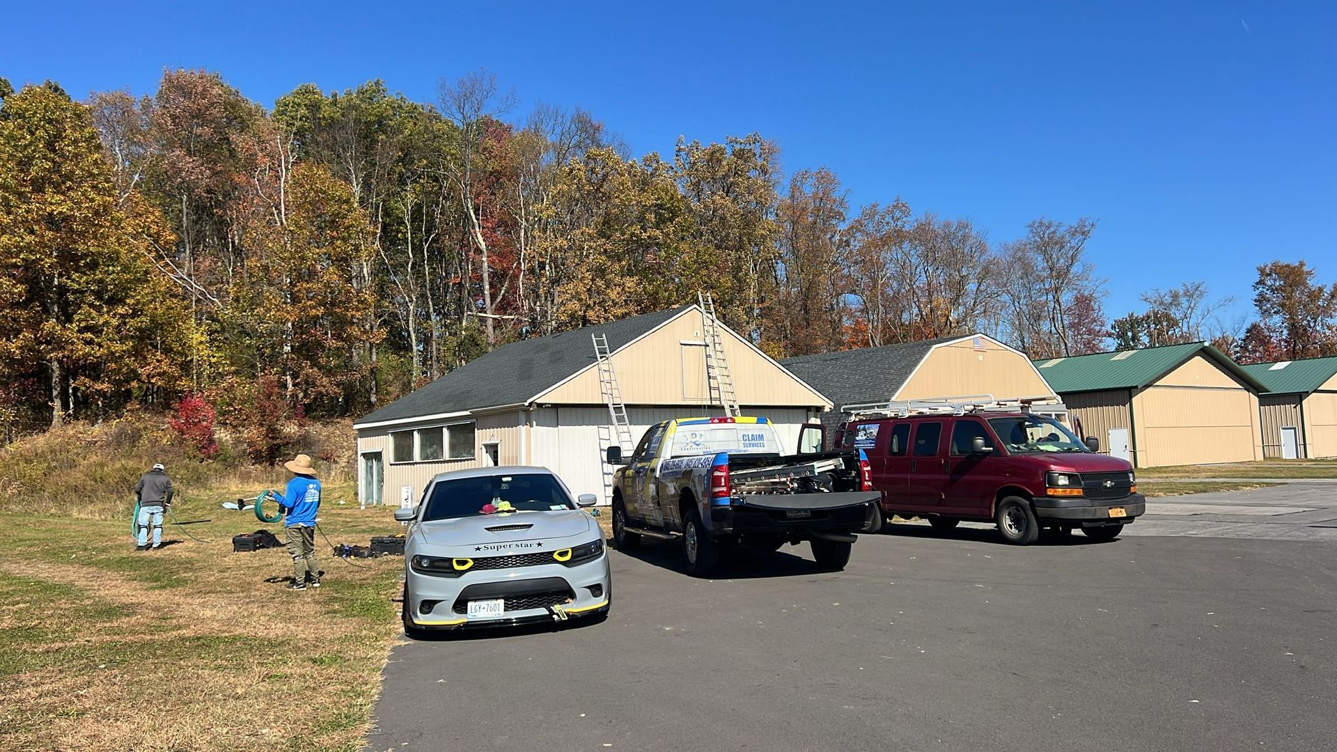 Cars parked near a building with people outside on a sunny day with fall foliage.