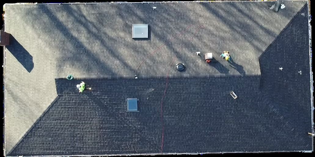 Overhead view of a dark shingled roof with various vents, chimneys, and shadows from trees.