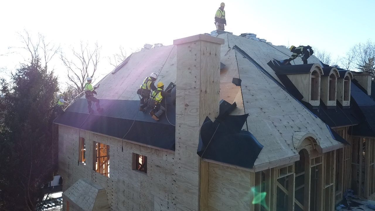 Construction workers on a roof installing shingles on a house.